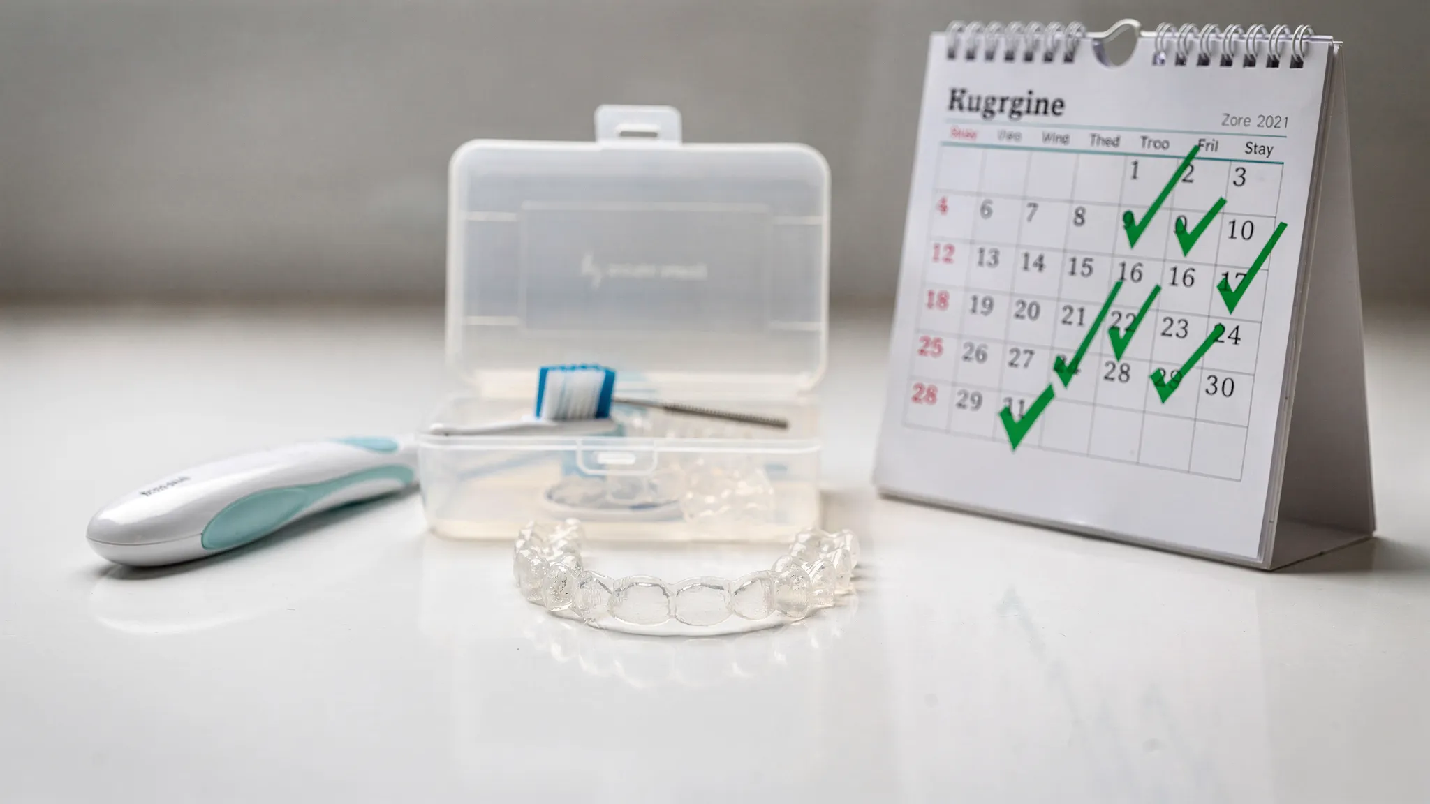 Un set de gutiere transparente lângă o cutie de transport, o periuță de dinți și un calendar cu zile bifate, sugerând disciplina zilnică de purtare și igienă.