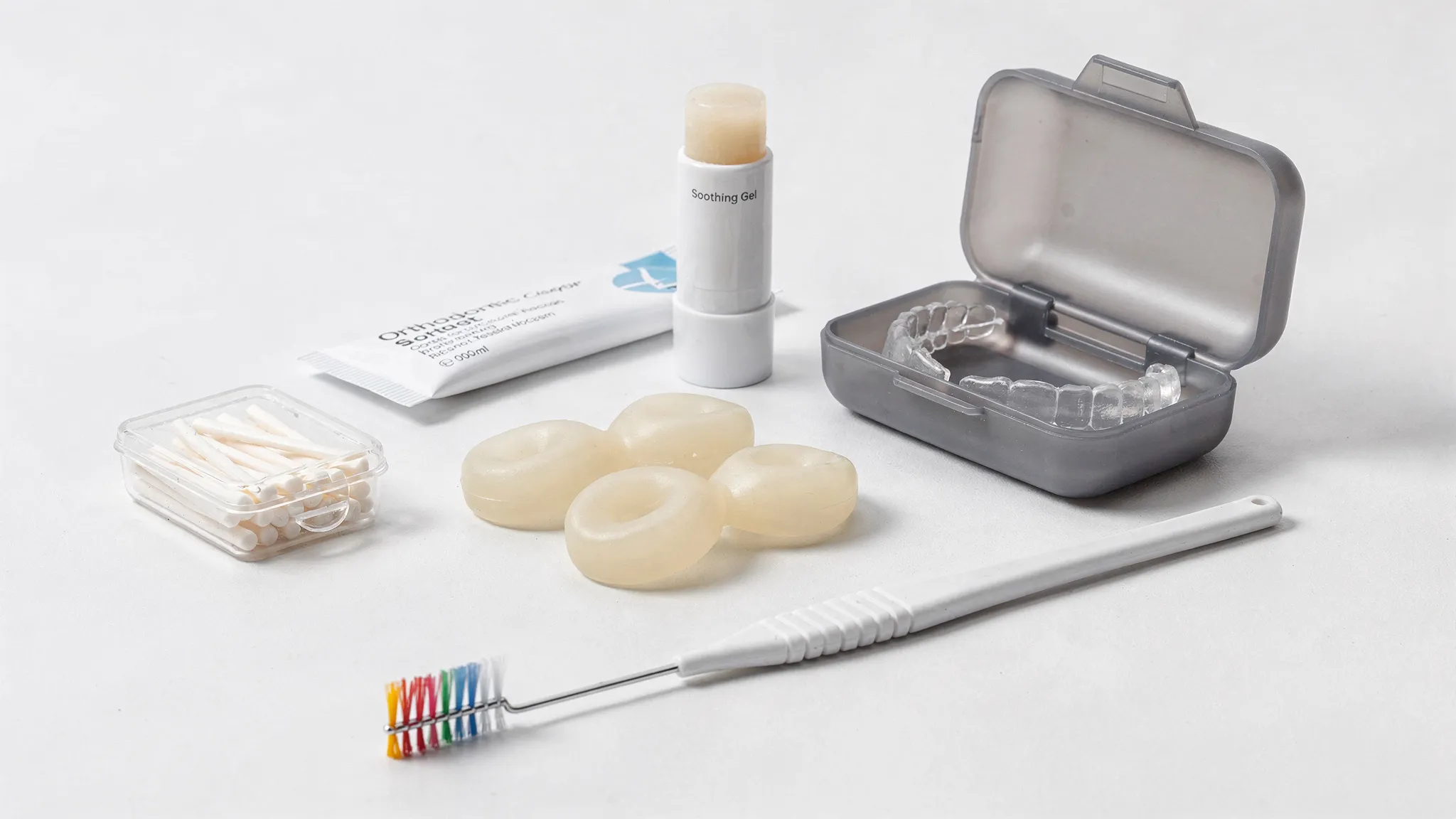 Un kit de confort ortodontic pe o suprafață curată, cu ceară ortodontică, gel pentru mucoasă, balsam de buze, cutie pentru alignere, chewies și o periuță interdentară, organizate simplu și igienic.