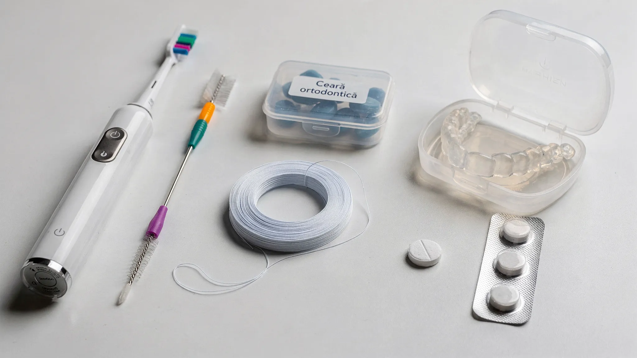 Un kit ortodontic organizat pe o masă curată, cu periuță interdentară, periuță electrică, ață dentară specială, ceară ortodontică, cutie pentru alignere și tablete de curățare pentru gutiere.