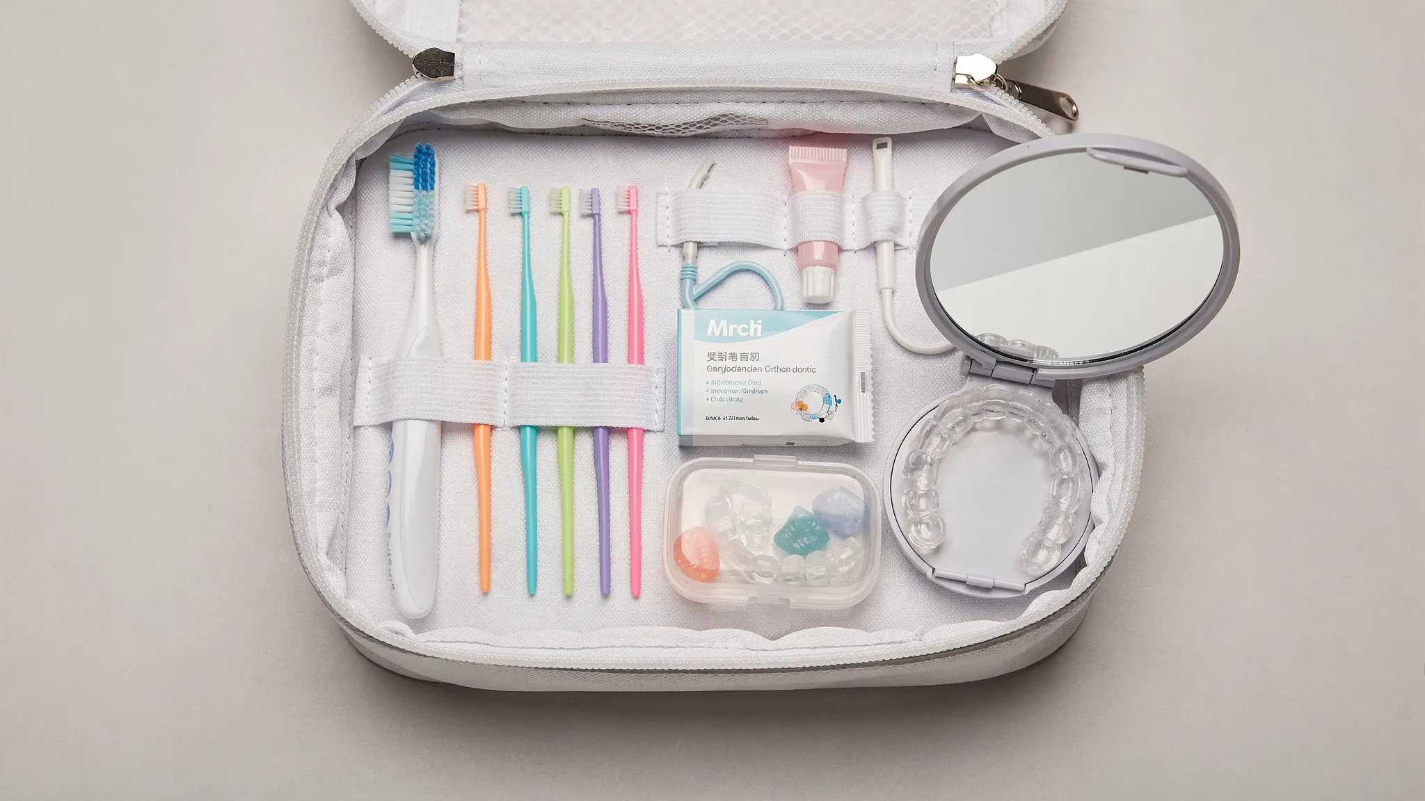 Un mini-kit ortodontic așezat într-o geantă, cu periuță de dinți de călătorie, pastă mică, periuțe interdentare, ceară ortodontică, cutie pentru alignere și oglindă compactă.